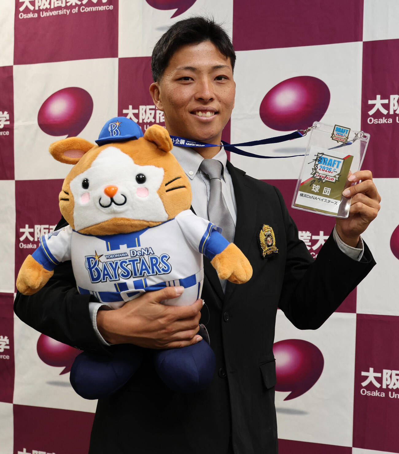 DeNA1位の大商大・星野世那は相川亮二監督のサイン入りパスとマスコットを手にポーズをとる（撮影・西尾就之）