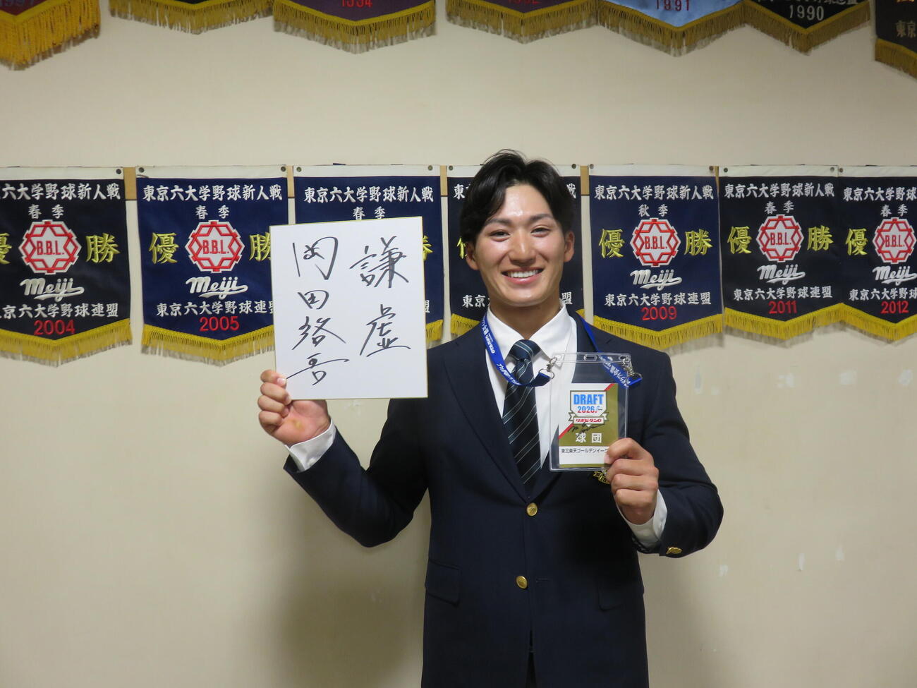 ドラフト2位指名を受けた明大・岡田啓吾内野手（右）は楽天から指名挨拶を受け、ドラフト会議の入館証をもらってにっこり。「謙虚」と座右の銘をしたたため（撮影・斎藤直樹）