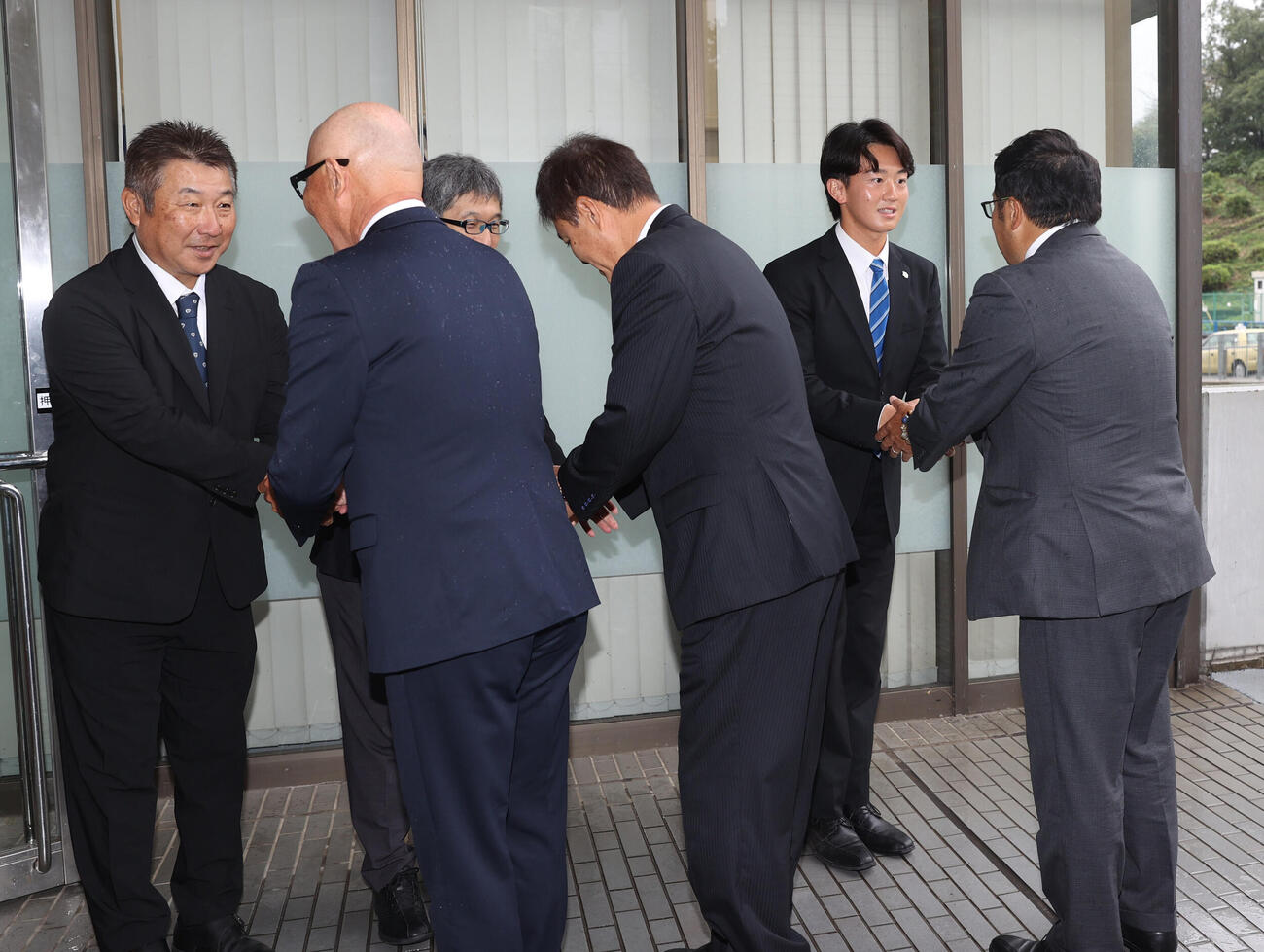 左から日体大野球部の古城隆利監督は阪神の畑山俊二統括スカウトと握手する、大石健二部長は平塚克洋スカウトと握手する、2位指名の日体大・馬場拓海は東辰弥編成ディレクターと握手する（撮影・柴田隆二）