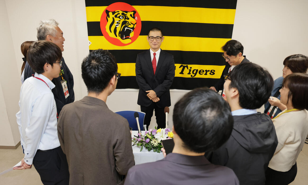 阪神の1軍打撃コーチに就任した坪井智哉氏は、虎のマークをバックに抱負を語る（撮影・宮崎幸一）