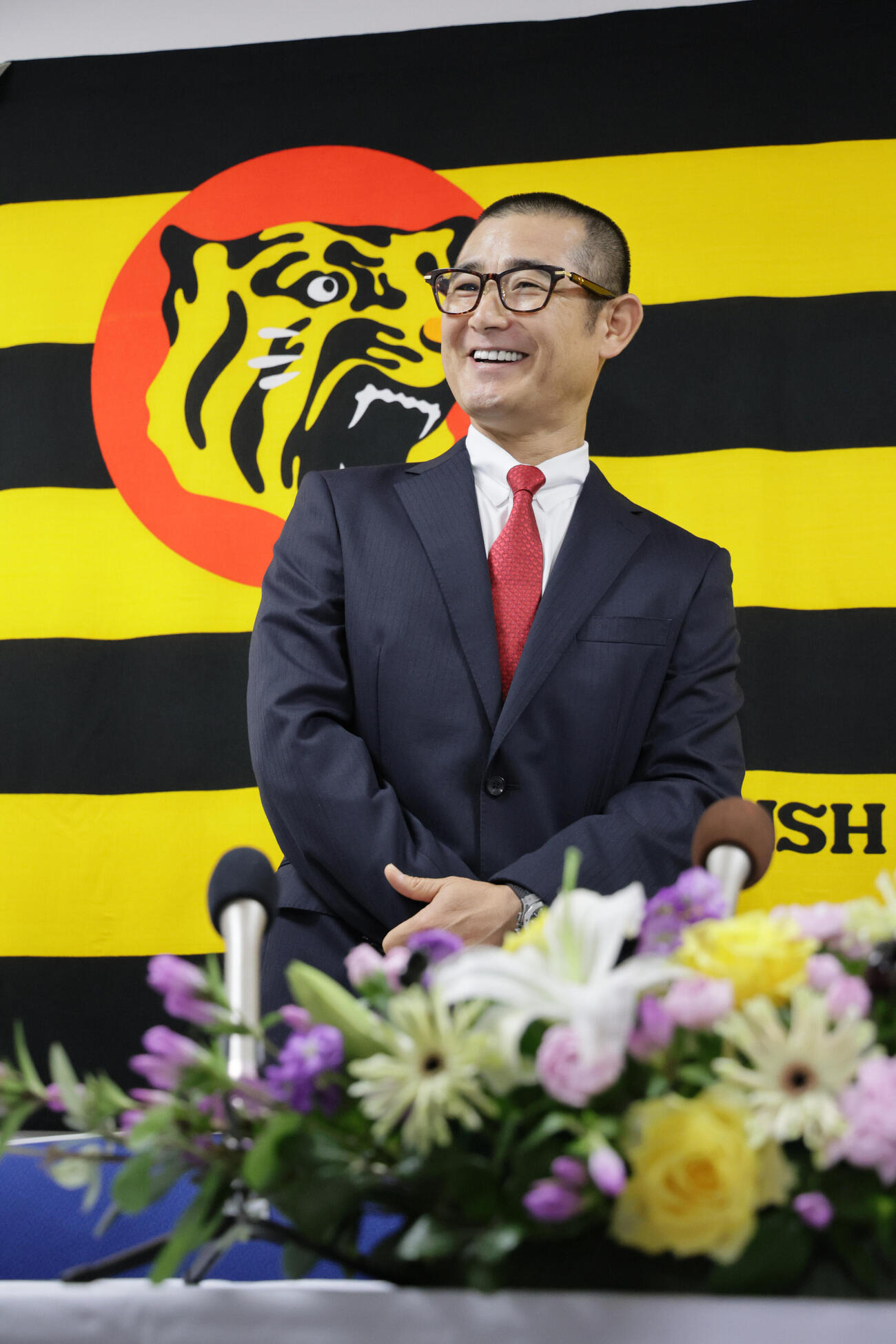 阪神の1軍打撃コーチに就任した坪井智哉氏は、虎のマークをバックに抱負を語る（撮影・宮崎幸一）