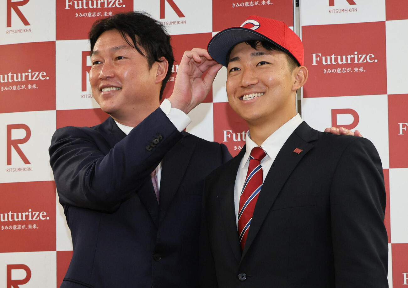 広島新井貴浩監督（左）の指名あいさつを受けた立命大・西野啓也は、広島の帽子をかぶり笑顔を見せる（撮影・宮崎幸一）