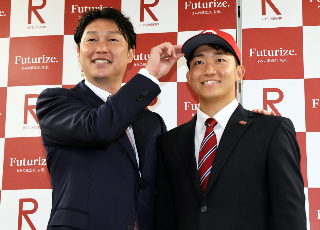 広島新井貴浩監督（左）の指名あいさつを受けた立命大・西野啓也は、広島の帽子をかぶり笑顔を見せる（撮影・宮崎幸一）