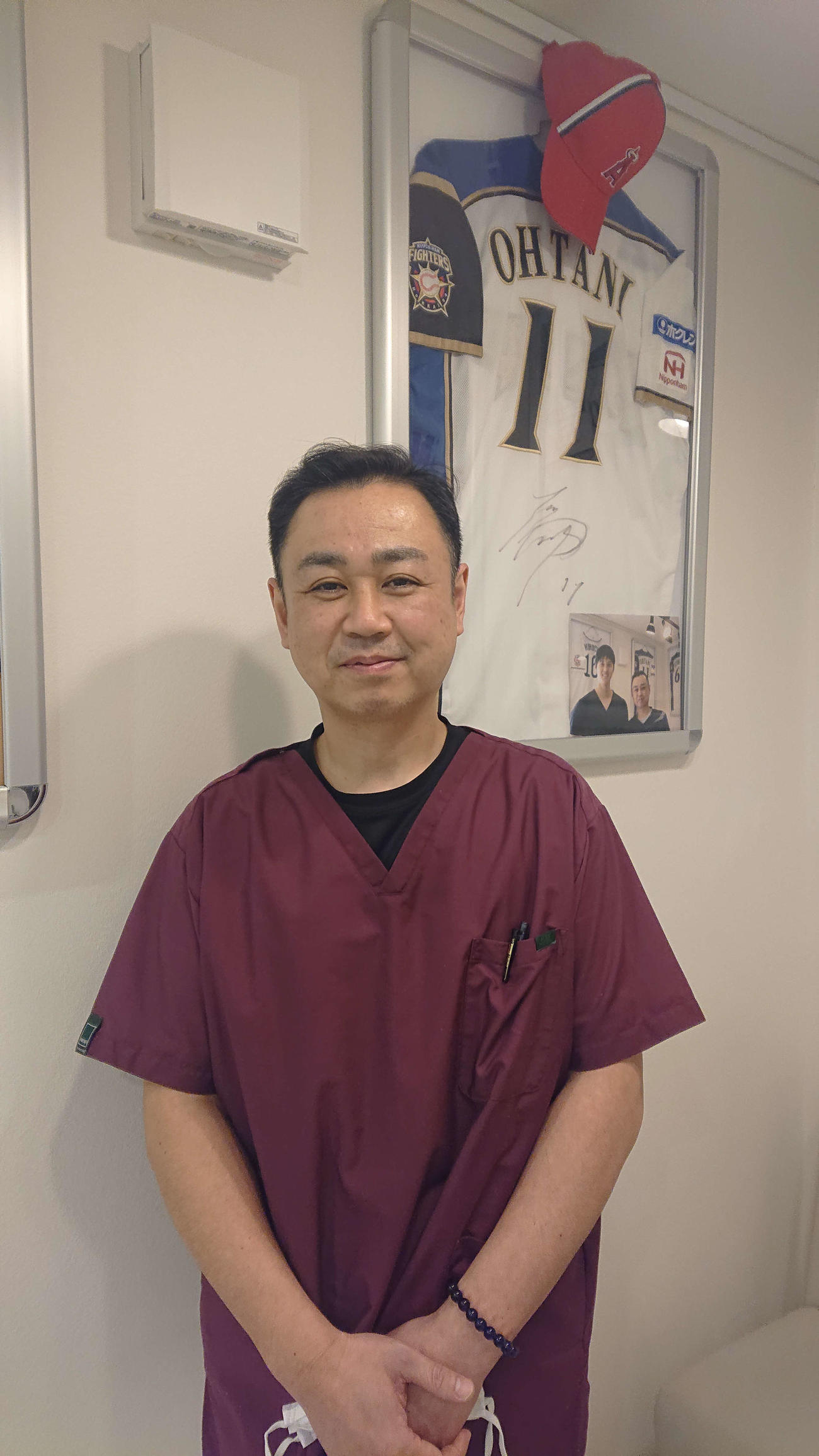 花巻市内に開業した「東北スポーツ整骨院」で大谷翔平選手のサイン入りのユニホームが飾られている前で笑顔を見せる花巻東時代のトレーナー・小菅智美氏（2021年12月14日撮影）