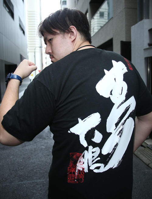 大鵬の書が記されたTシャツを披露する納谷幸男（撮影・中島郁夫）