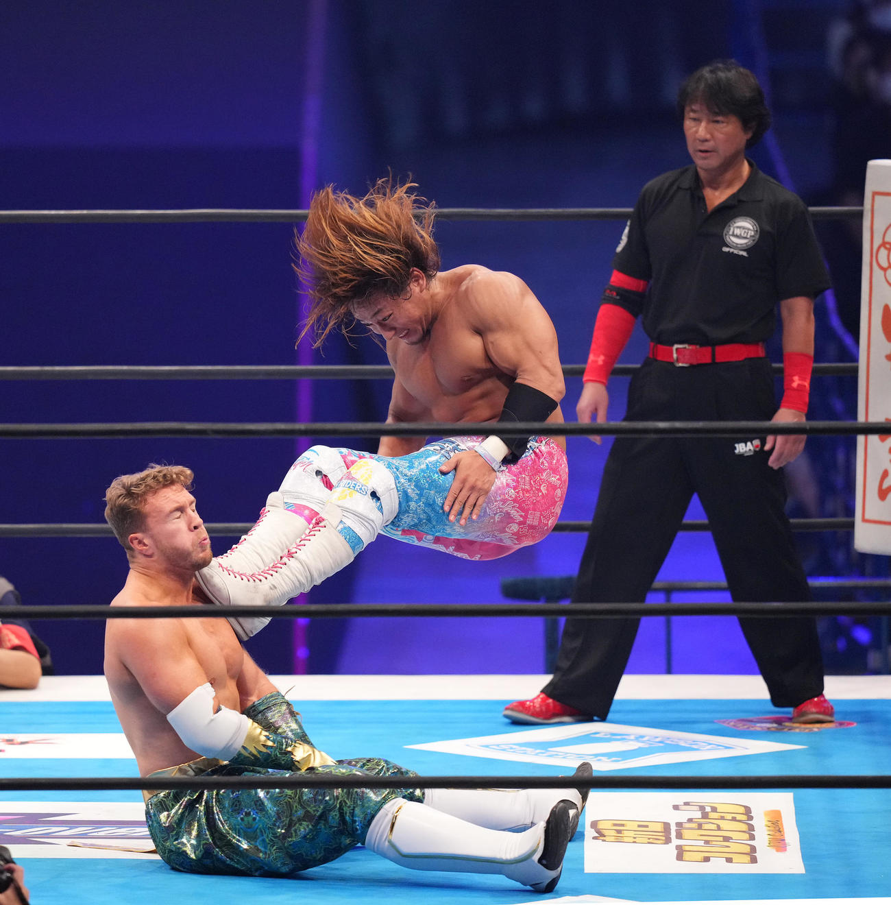 2022年11月20日、実父のレッドシューズ海野レフェリー（奥）が見つめる前でオスプレイ（左）にキックをさく裂する海野（撮影・菅敏）