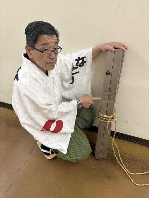 土俵築の監督を務めている呼び出しの吾郎。1尺8寸を意味する18のメモリを指さしている