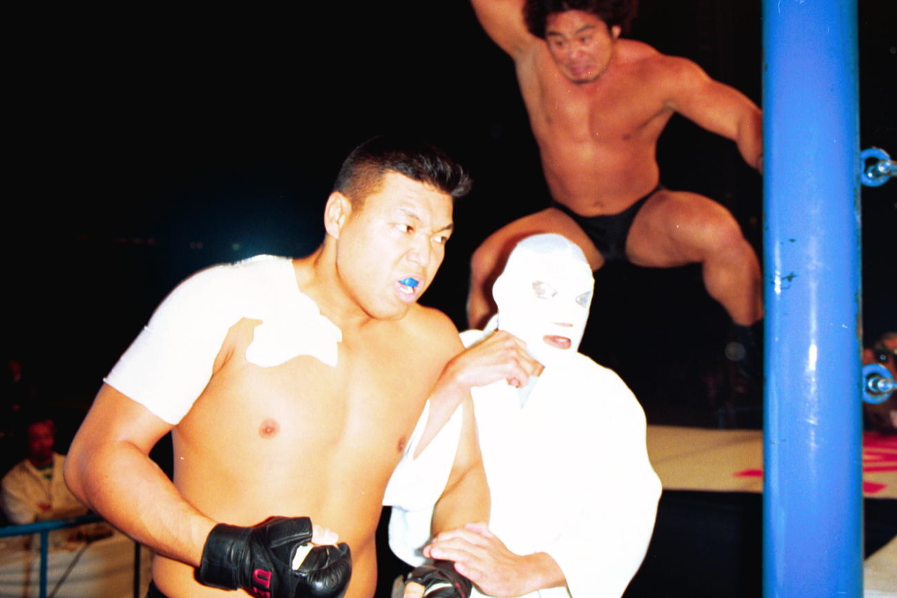 小川直也（左）と覆面（右・アントニオ猪木）を後ろから襲う中西学