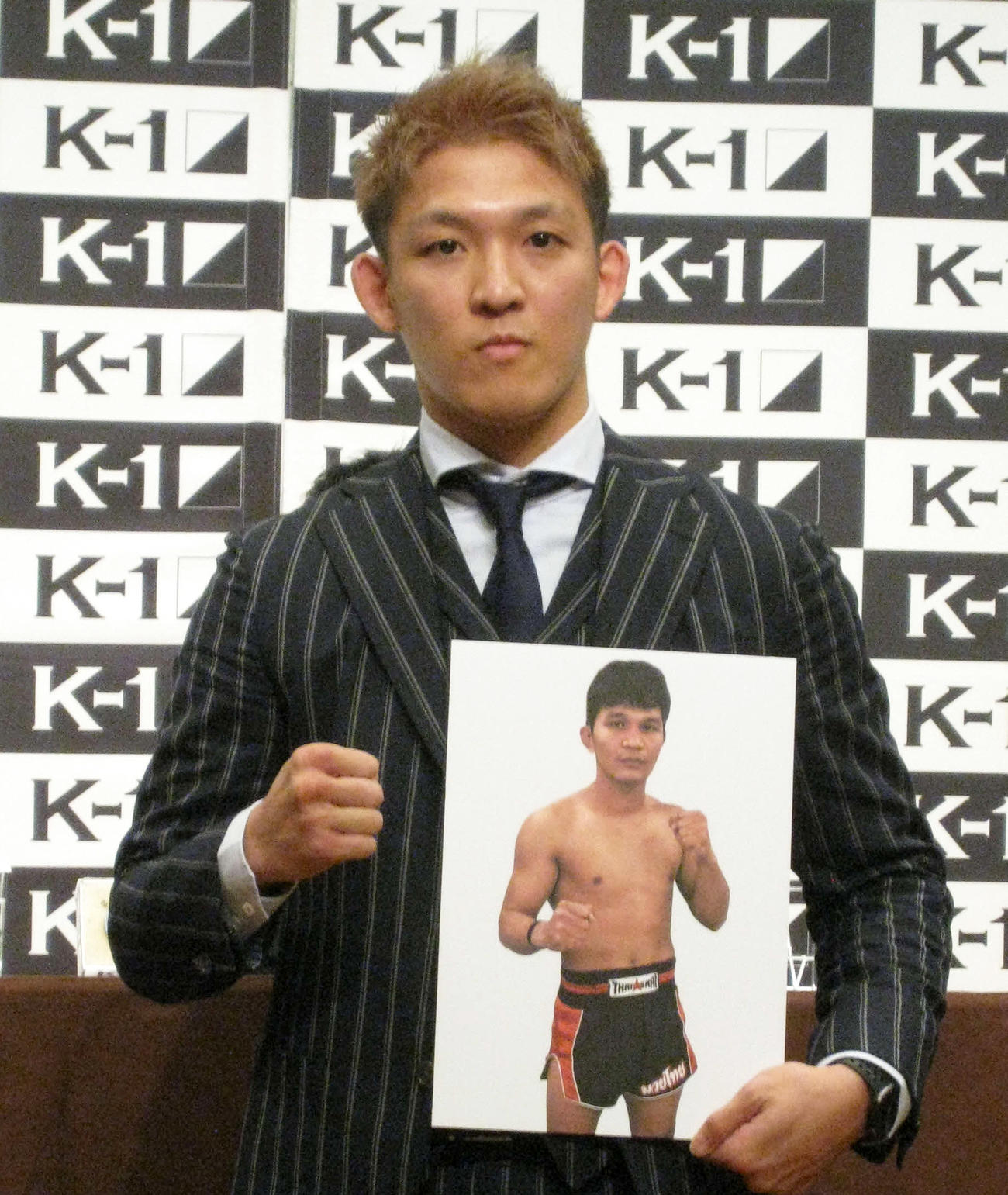 対戦相手ソーシーソムポンのパネルを持ち、拳に力を込める野杁正明（撮影・吉池彰）