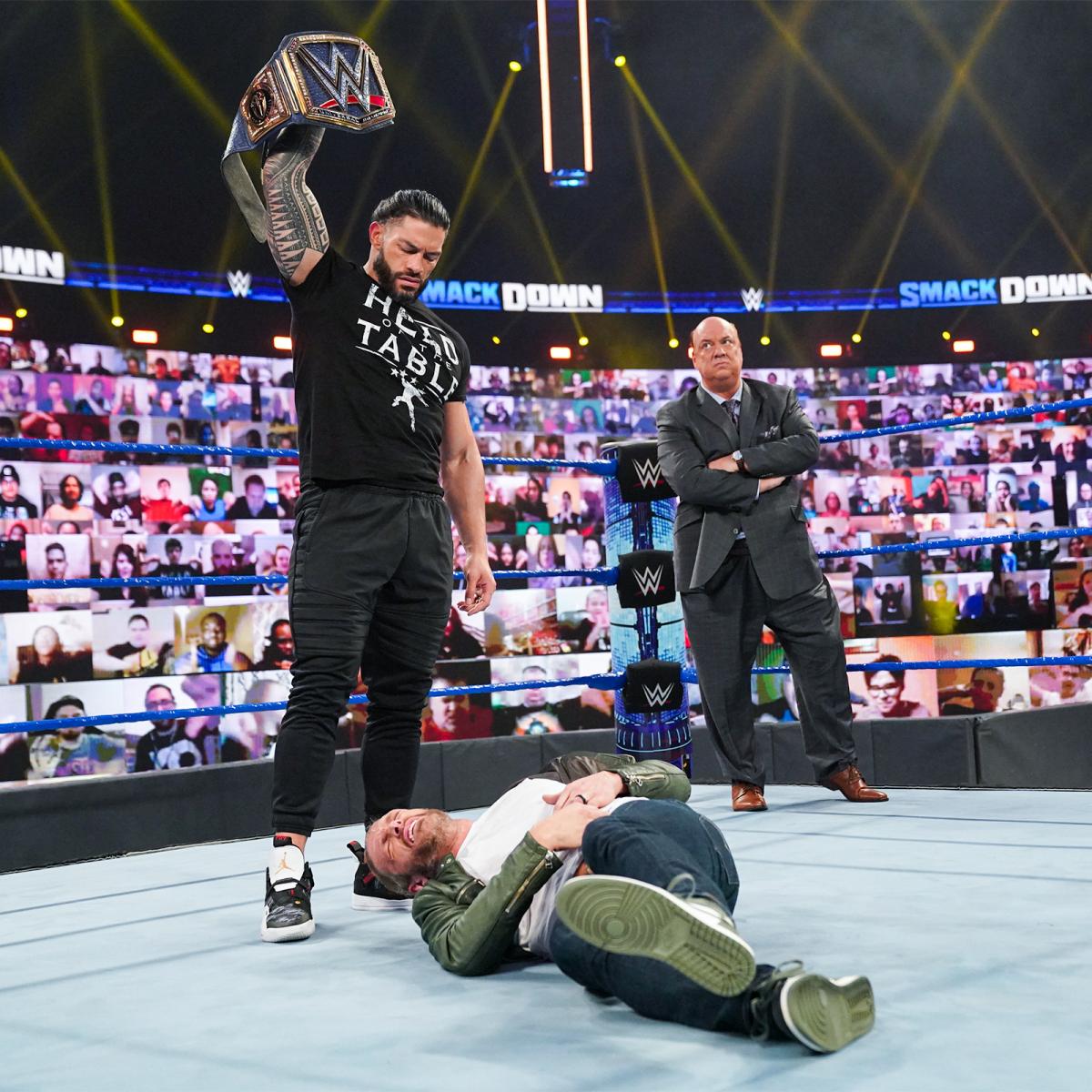 倒れたエッジ（手前）にWWEユニバーサル王座ベルトを掲げる王者ローマン・レインズ。右奥はポール・ヘイマン（C）2021 WWE, Inc. All Rights Reserved.