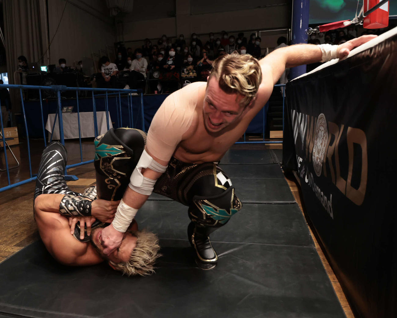 新日本プロレス後楽園大会　場外でSANADA（下）の鼻をつかみ、押さえ付けるウィル・オスプレイ（新日本プロレス提供）