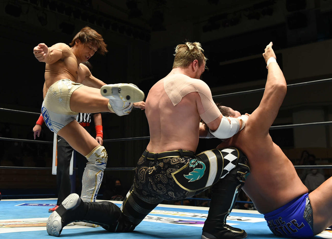 新日本プロレス後楽園大会　ウィル・オスプレイ（中央）の背中に蹴りを入れる飯伏幸太（左）（新日本プロレス提供）