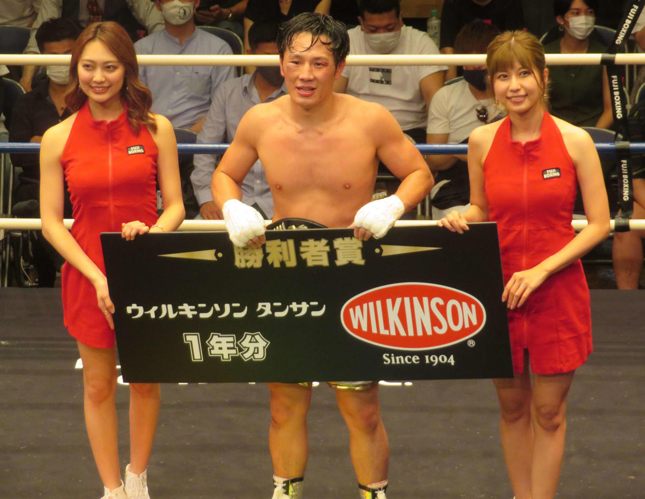 ラウンドガールとともに勝利賞のボードを手にする日本スーパーライト級新王者鈴木