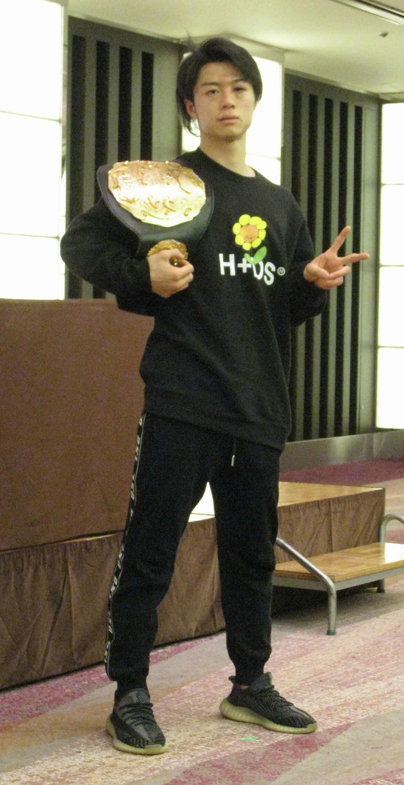 ベルトを肩にVサインの金子晃大（撮影・吉池彰）