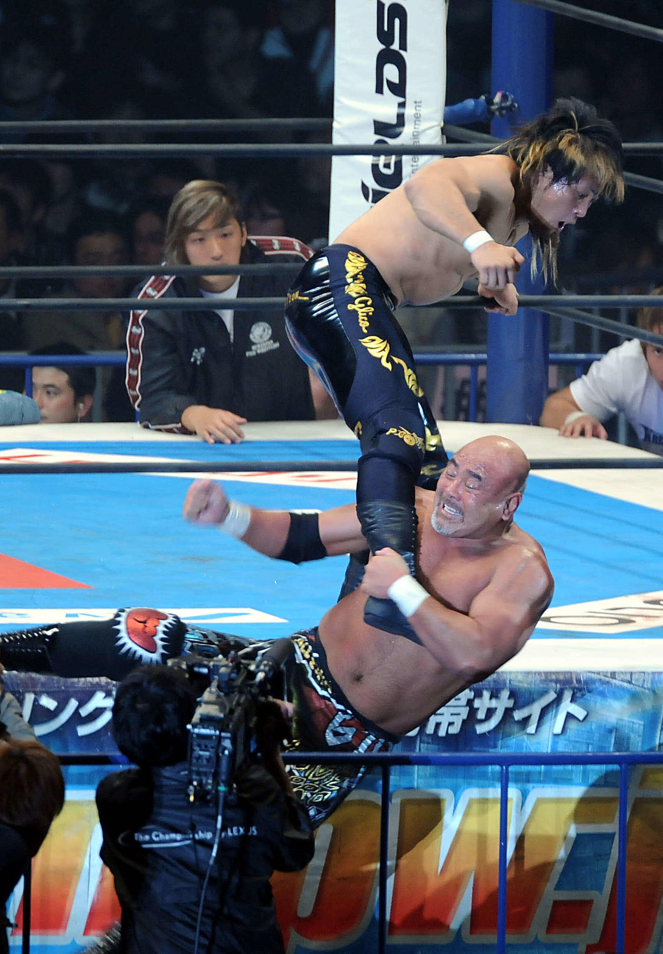 新日本東京ドーム大会IWGPヘビー級選手権　棚橋弘至対武藤敬司　エプロンに立つ棚橋弘至（上）へドラゴンスクリューを見舞う武藤敬司　