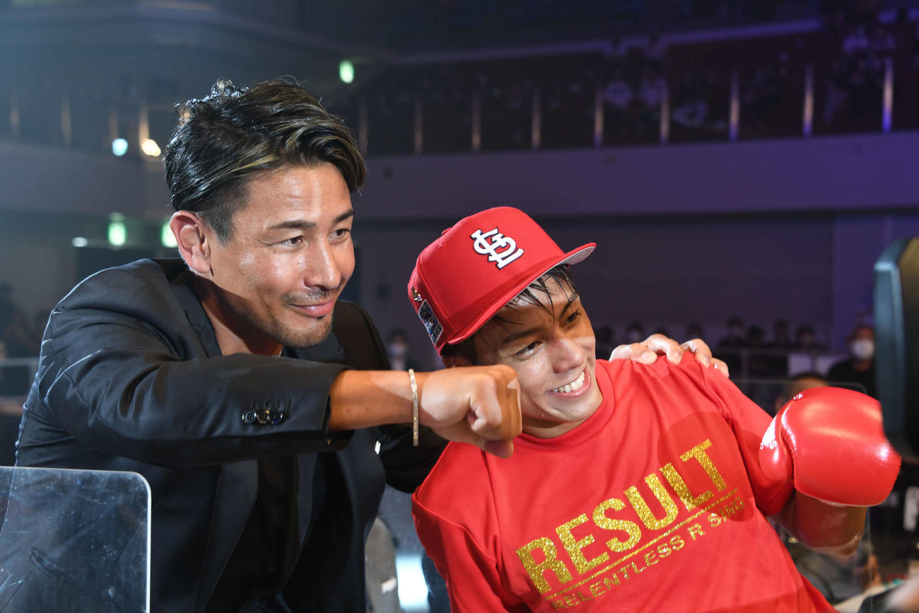 石井一成（右）は解説席の魔裟斗と笑顔でポーズする