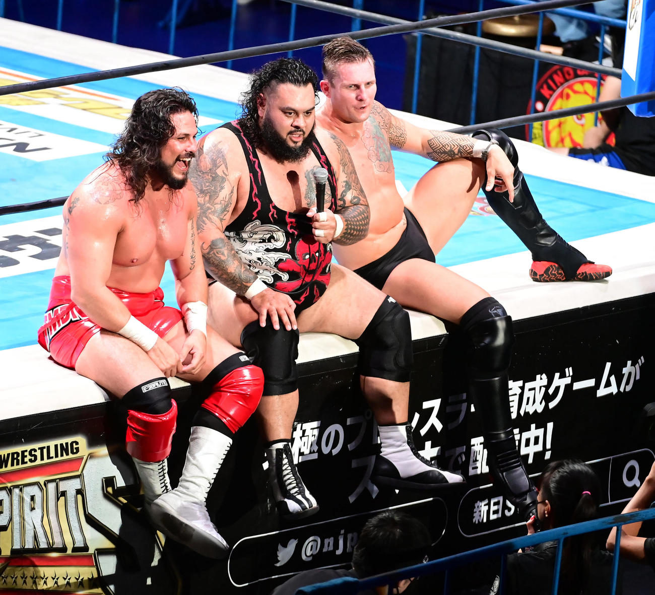 矢野、棚橋、オカダ・カズチカ対バッド・デュード・ティト、シェイン・ヘイスト、JONAH 6人タッグ戦で勝利しエプロンに座りマイクでアピールするJONAH。左はバッド・デュード・ティト、右はシェイン・ヘイスト（撮影・小沢裕）