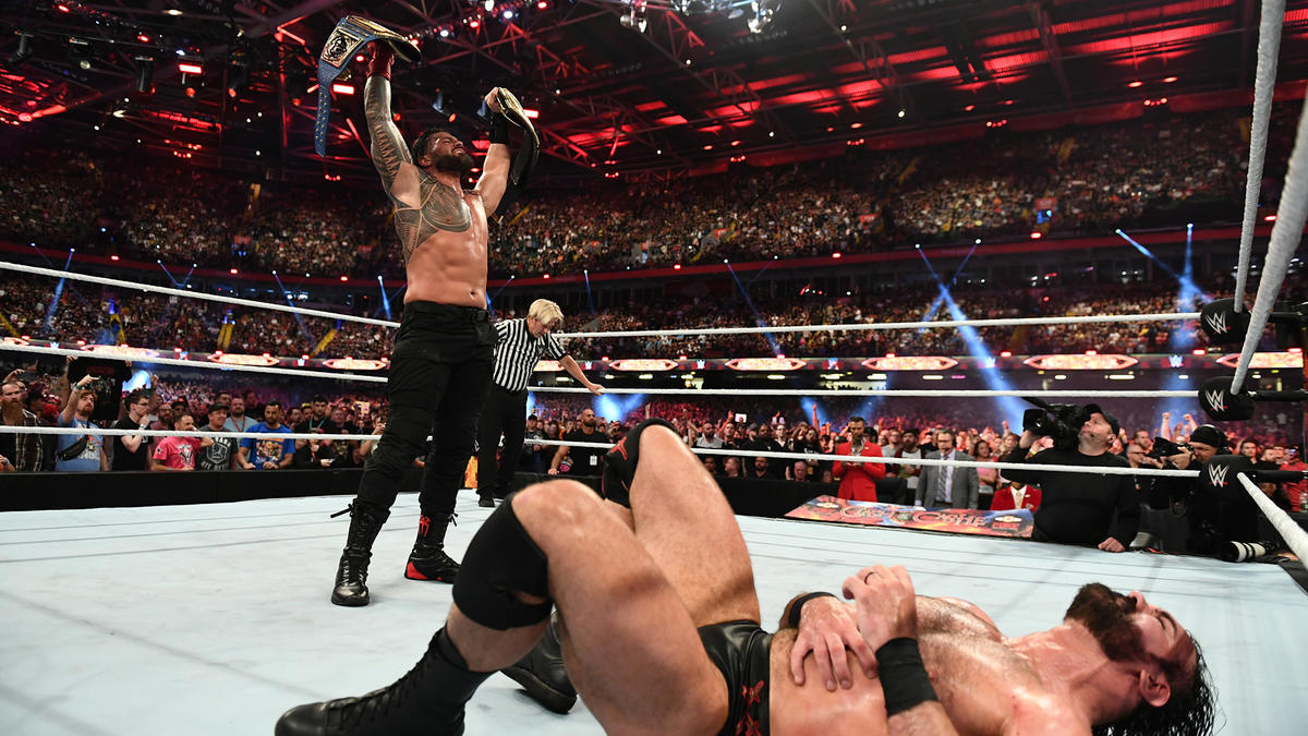 撃破したドリュー・マッキンタイア（手前）を見下し、WWEヘビー、ユニバーサル王座の2本のベルトを掲げた統一王者ローマン・レインズ（C）2022 WWE, Inc. All Rights Reserved.