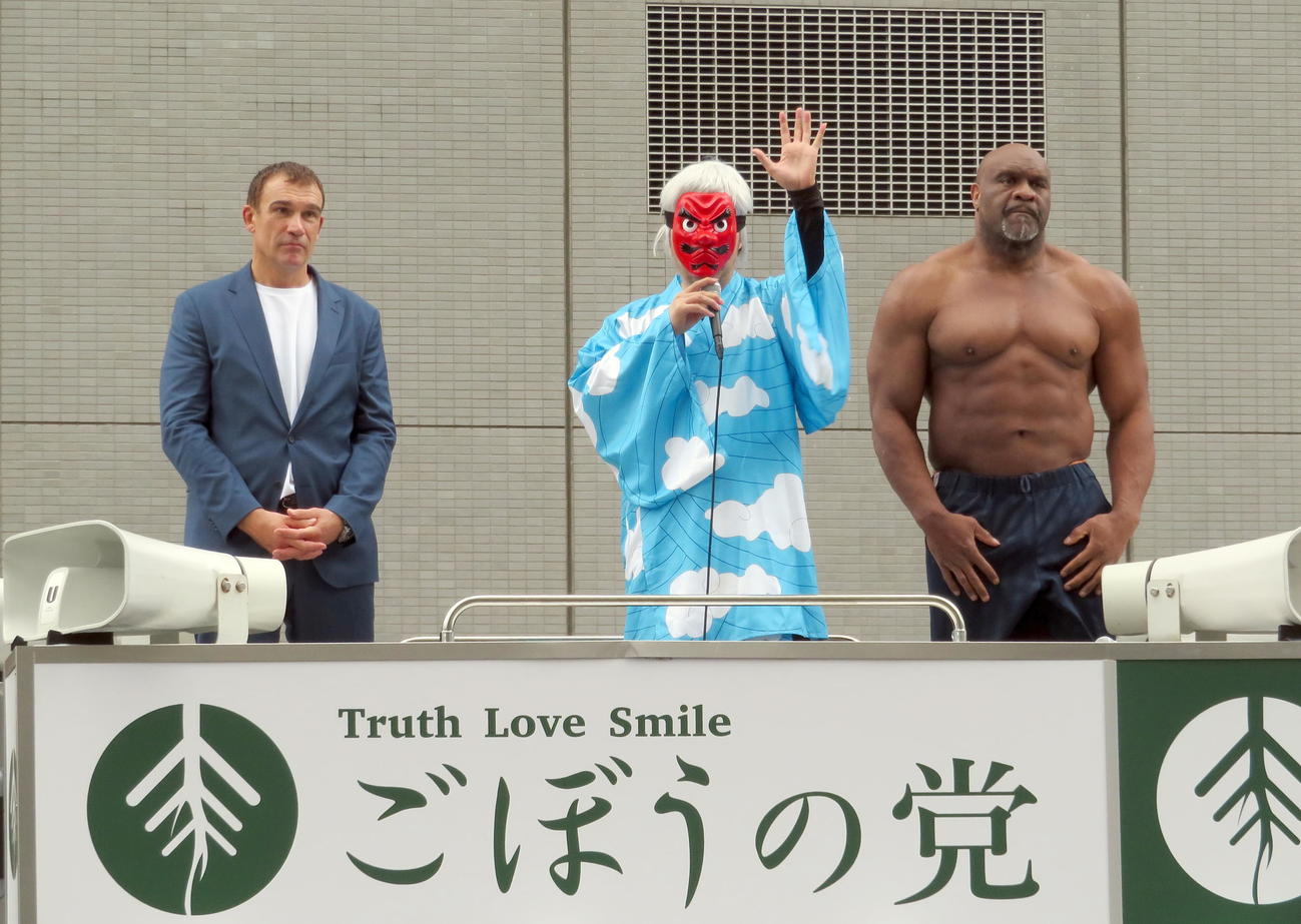 ピーター・アーツ（左）とボブ・サップ（右）をゲストに迎えて都庁前で所信表明演説を行うごぼうの党の奥野卓志代表。人気アニメ「鬼滅の刃」の鱗滝左近次のような格好で登壇した（2022年6月23日撮影）
