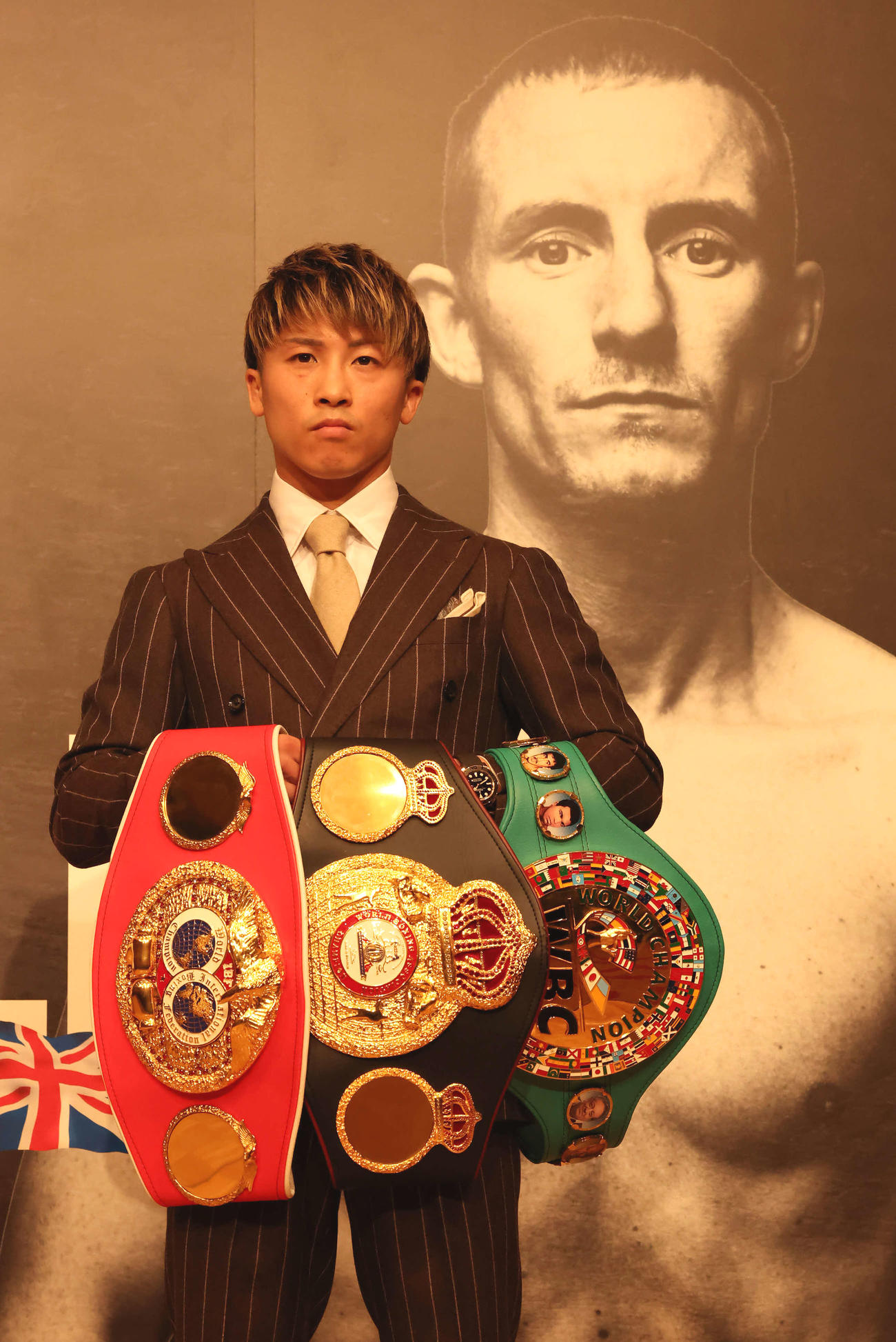 3本のベルトを手に対戦相手ポール・バトラーの写真の前で写真に納まる井上（2022年10月13日撮影）