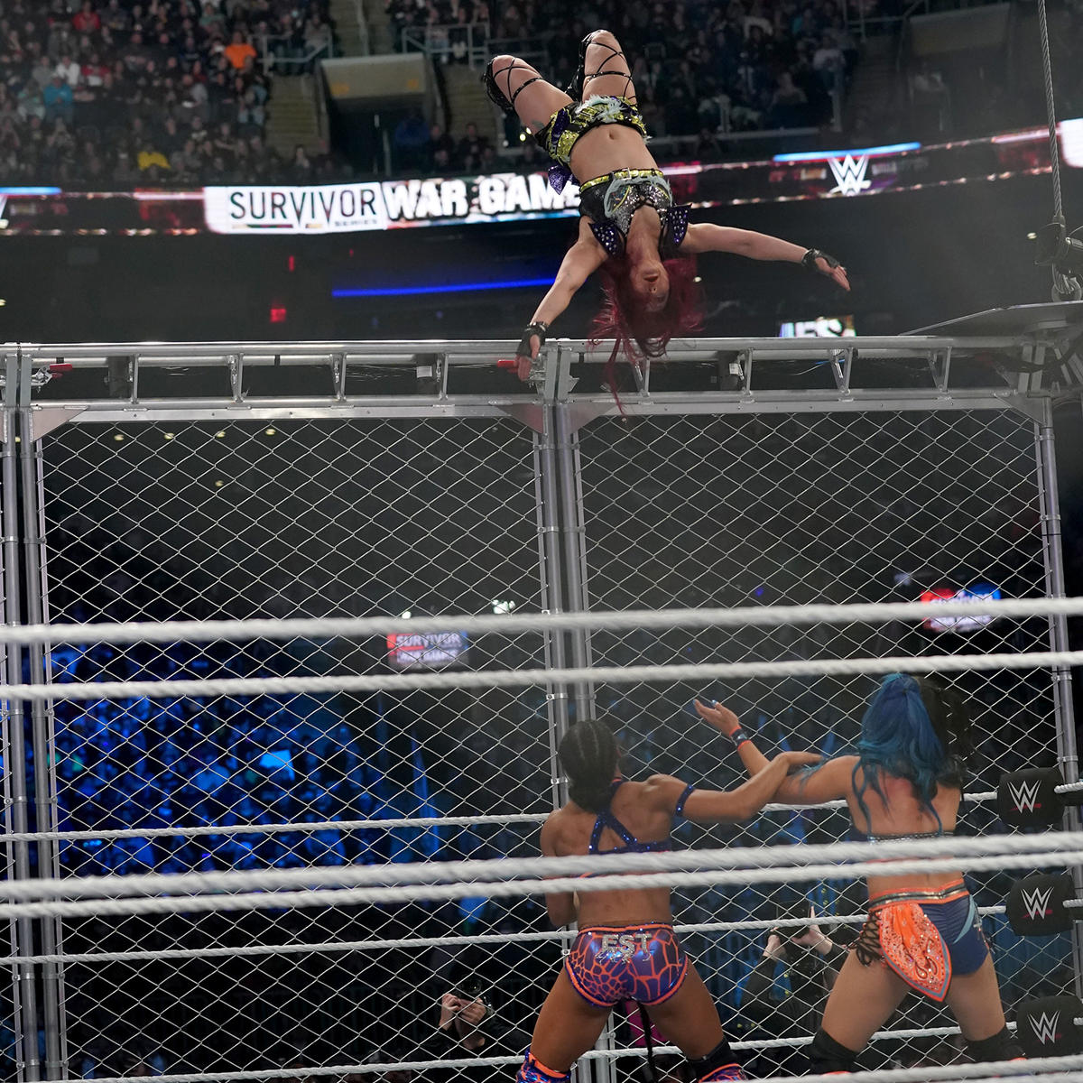 ケージ上からビアンカ・ブレア（左下）、ミア・イム（右下）に月面水爆を狙うイヨ・スカイ（C）2022 WWE, Inc. All Rights Reserved.