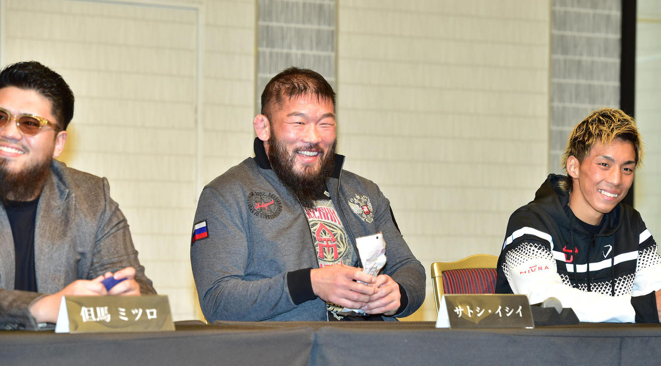 前日会見、ほかの対戦カードの選手が挑発で出してきたサラダチキンを名乗り出て受け取りうれしそうにするサトシ・イシイ（中央）（撮影・清水貴仁）