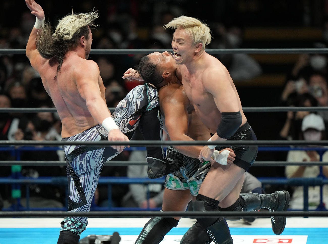 アーロン・ヘナーレ（中央）にVトリガーとレインメーカーをさく裂させるケニー・オメガ（左）とオカダ・カズチカ（撮影・狩俣裕三）