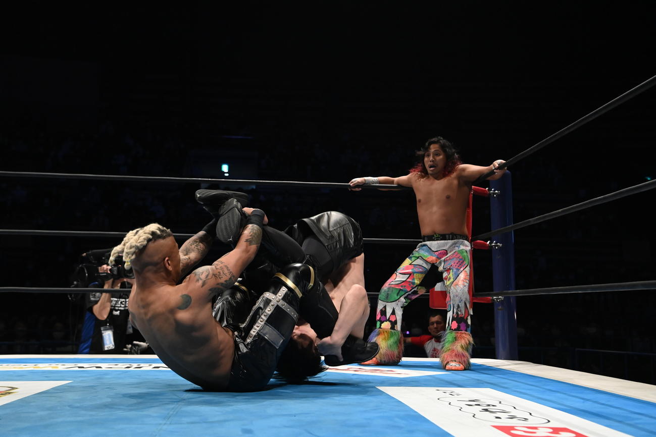 コーナーの高橋ヒロム（右）へ、アクロバティックな動きで攻撃をしかけるリオ・ラッシュ（左）とYOU（新日本プロレス提供）