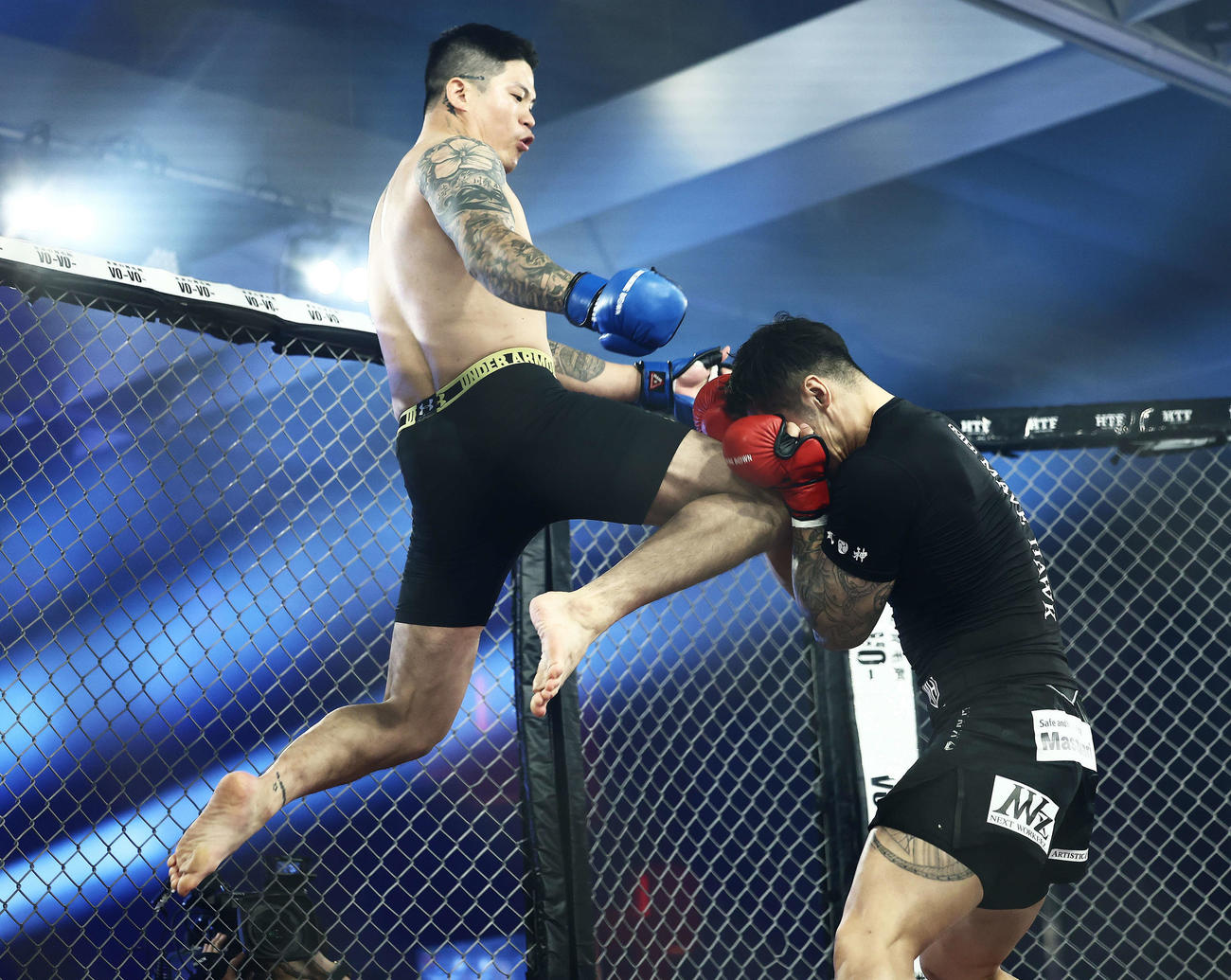 パク・ウォンシク（左）の飛び膝蹴りに耐える飯田将成（撮影・河田真司）