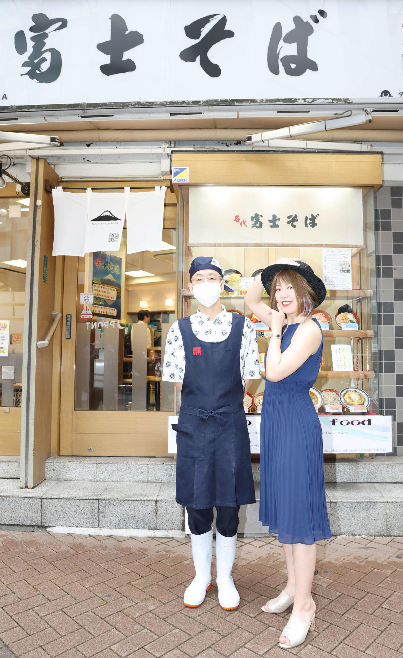 富士そばを訪れ、貴婦人ポーズを取り、店長と記念写真に納まる桜井まい（撮影・宮地輝）
