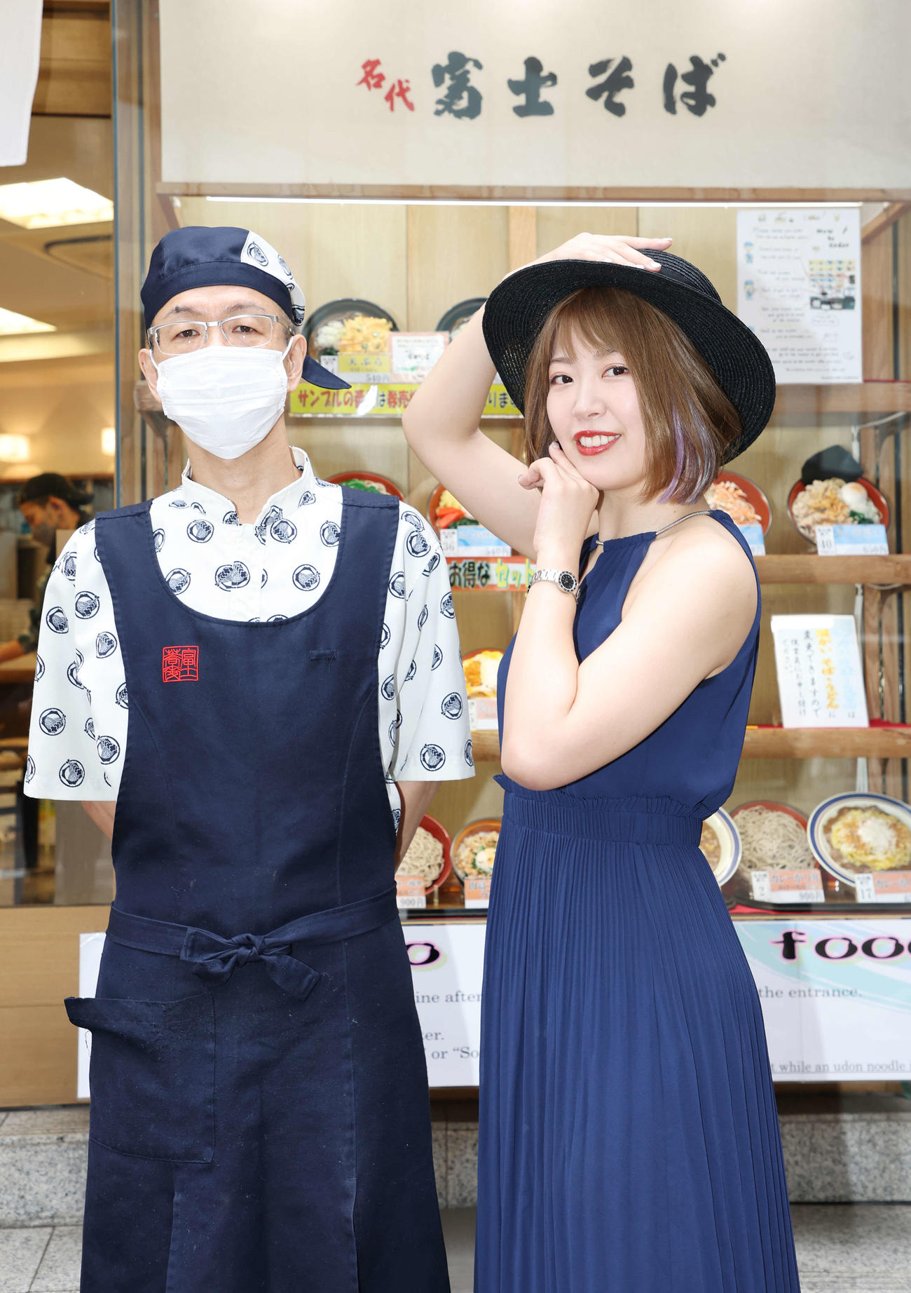 富士そばを訪れ、貴婦人ポーズを取り、店長と記念写真に納まる桜井まい（撮影・宮地輝）