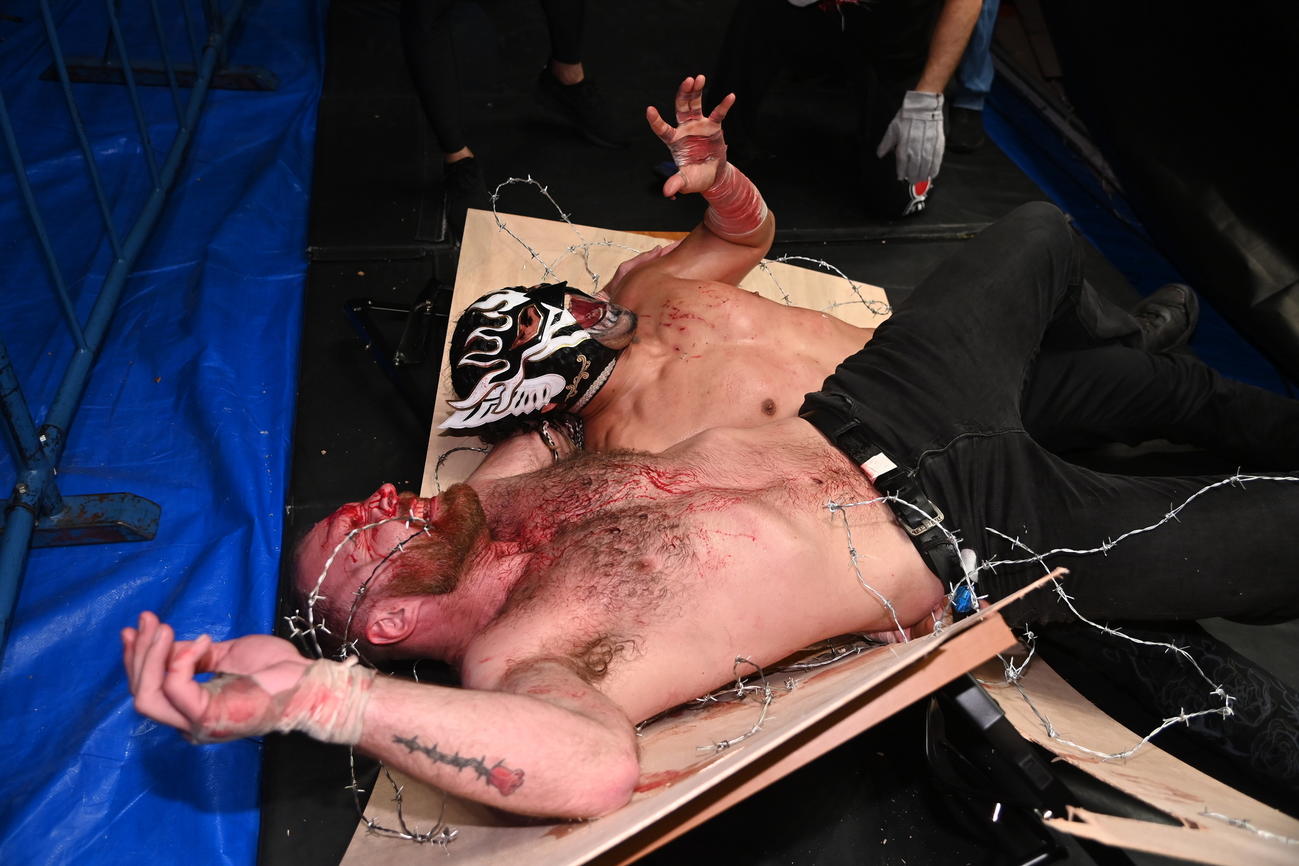 有刺鉄線ボードの上で悶絶するエル・デスペラードとジョン・モクスリー（手前）（新日本プロレス提供）