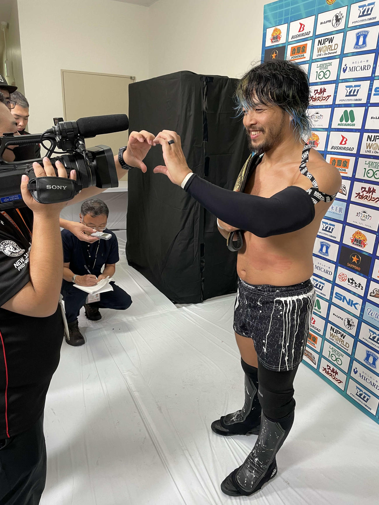 試合後のバックステージで新日本の、“いつもの”カメラマンと手でハートマークをつくるKENTA