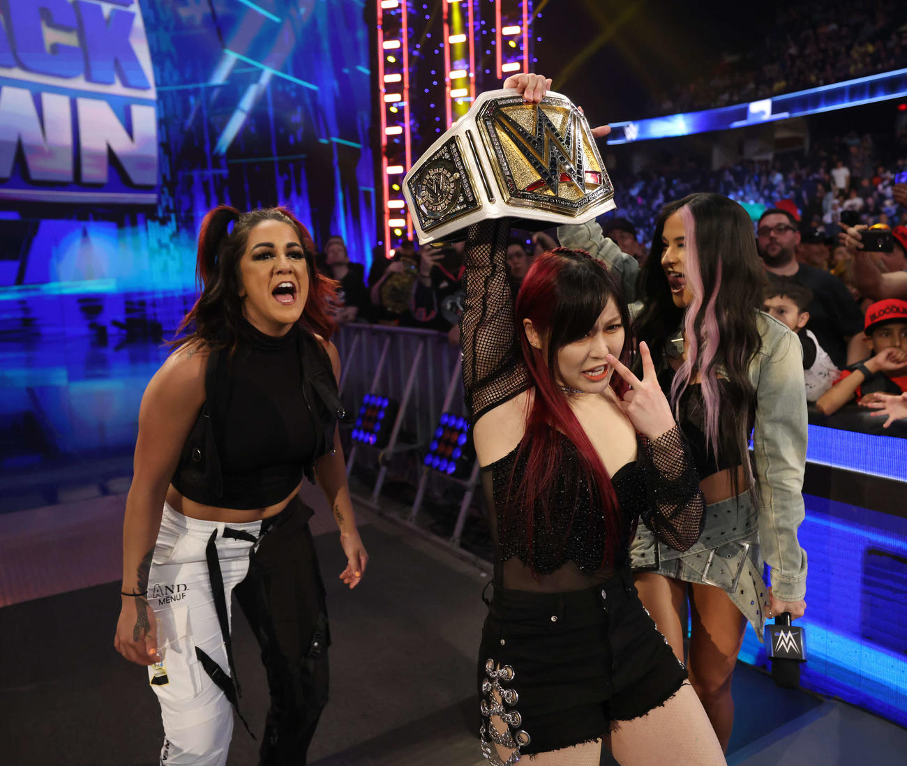 WWE女子王座ベルトを持って入場する王者イヨ・スカイ（中央）。ベイリー（左端）、ダコタ・カイとともに花道を歩く（C）2023 WWE, Inc. All Rights Reserved.
