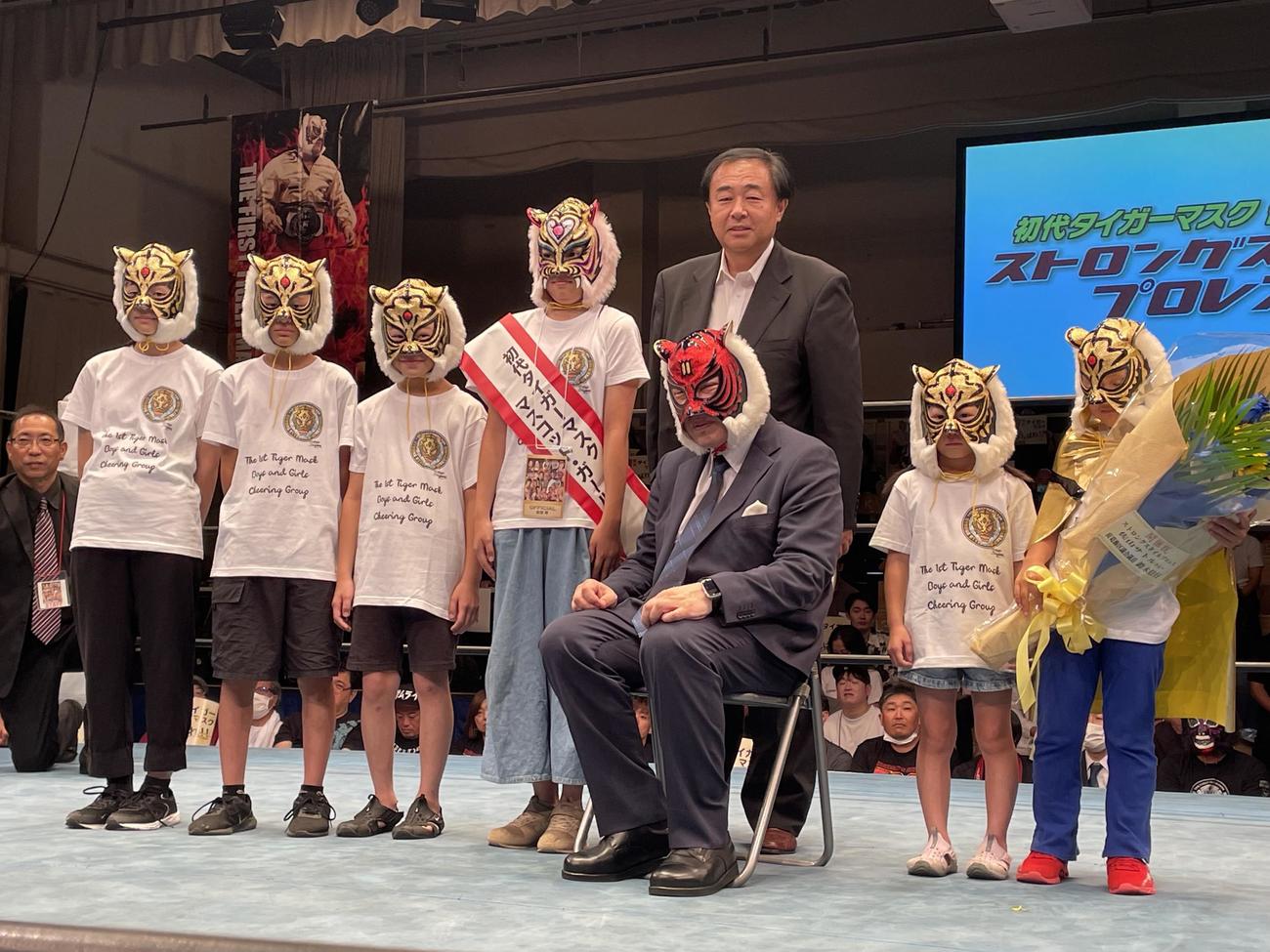 自身が主宰するストロングスタイルプロレス後楽園ホール大会で、初代タイガーマスク応援少年少女、マスコット・ガールと、椅子に座って記念撮影に応じる初代タイガーマスクの佐山サトル