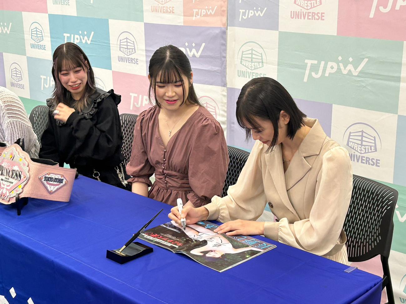 自身のグラビアが掲載された雑誌の上にチーム名を書く長野じゅりあ。左は乃蒼ヒカリ、中央は宮本もか（東京女子プロレス提供）