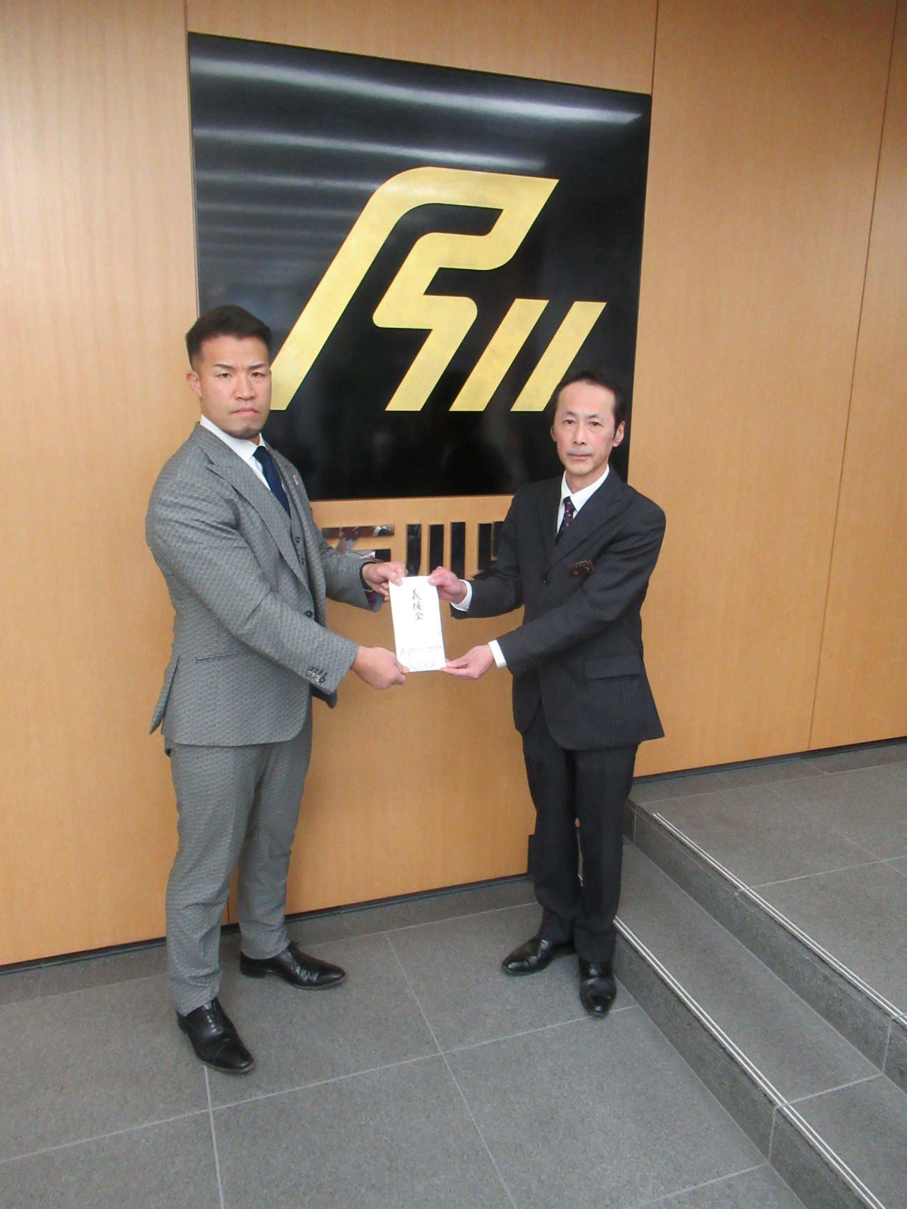 大阪プロレスのゼウス社長（左）は、義援金100万円を、石川県大阪事務所の山下幸則所長に手渡しした（撮影・益田一弘）