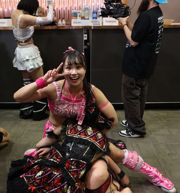 東京女子プロレス　場外で伊藤麻希と、山下実優を押さえ込み、カメラにポーズを決める渡辺未詩。奥はビールを購入する辰巳リカ（東京女子プロレス提供）