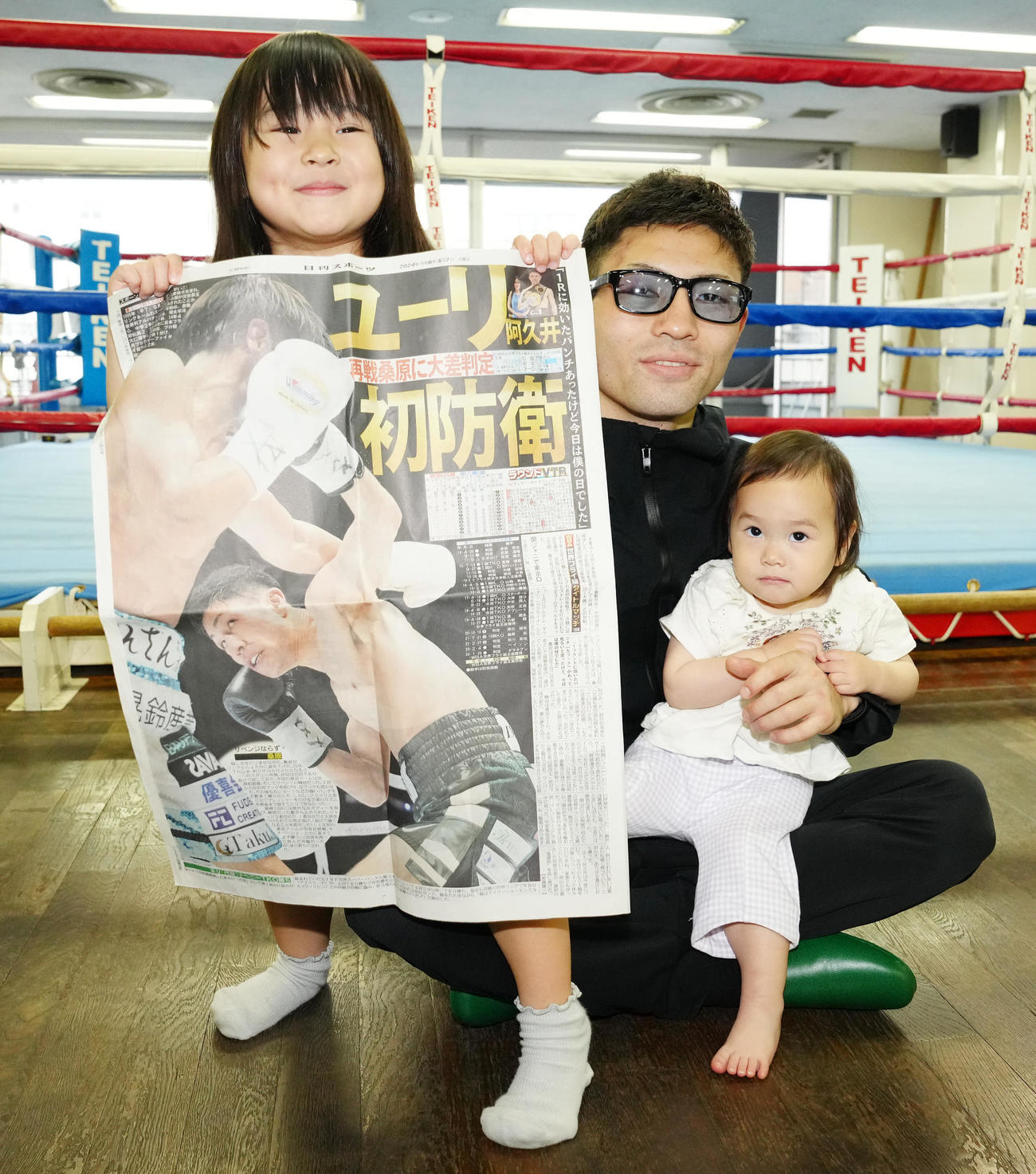 初防衛から一夜明け、子どもと写真に納まるユーリ阿久井（中央）。左は本紙を手にする長女の千聖ちゃん、右は次女の琴乃ちゃん（撮影・江口和貴）