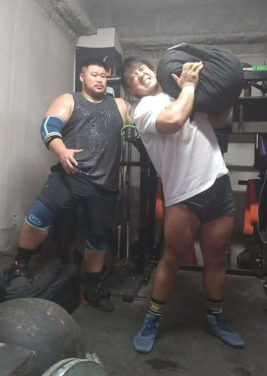 100キロの砂袋を抱え上げる稲村愛輝、左は指導する日本ストロングマン協会の中嶋健詞代表