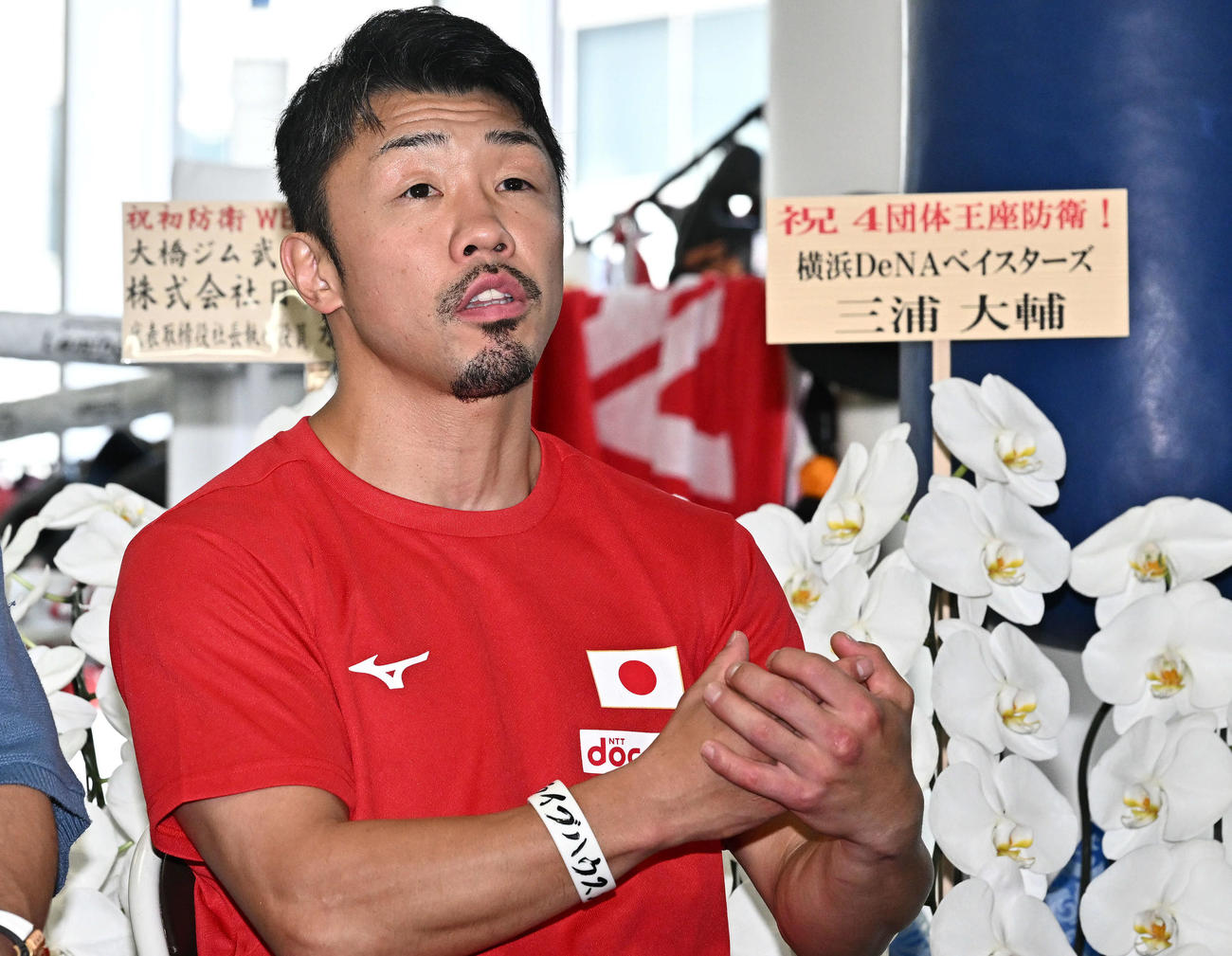 DeNA三浦監督から届いた花の前で一夜明け会見する八重樫トレーナー（撮影・滝沢徹郎）　