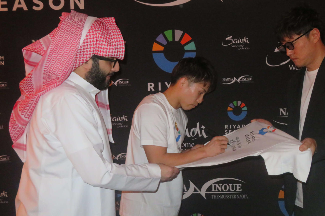 11月4日、リヤド・シーズンのロゴ入りTシャツにサインする井上尚弥（中央）。左がサウジアラビア総合娯楽庁のトゥルキ・アラルシク長官