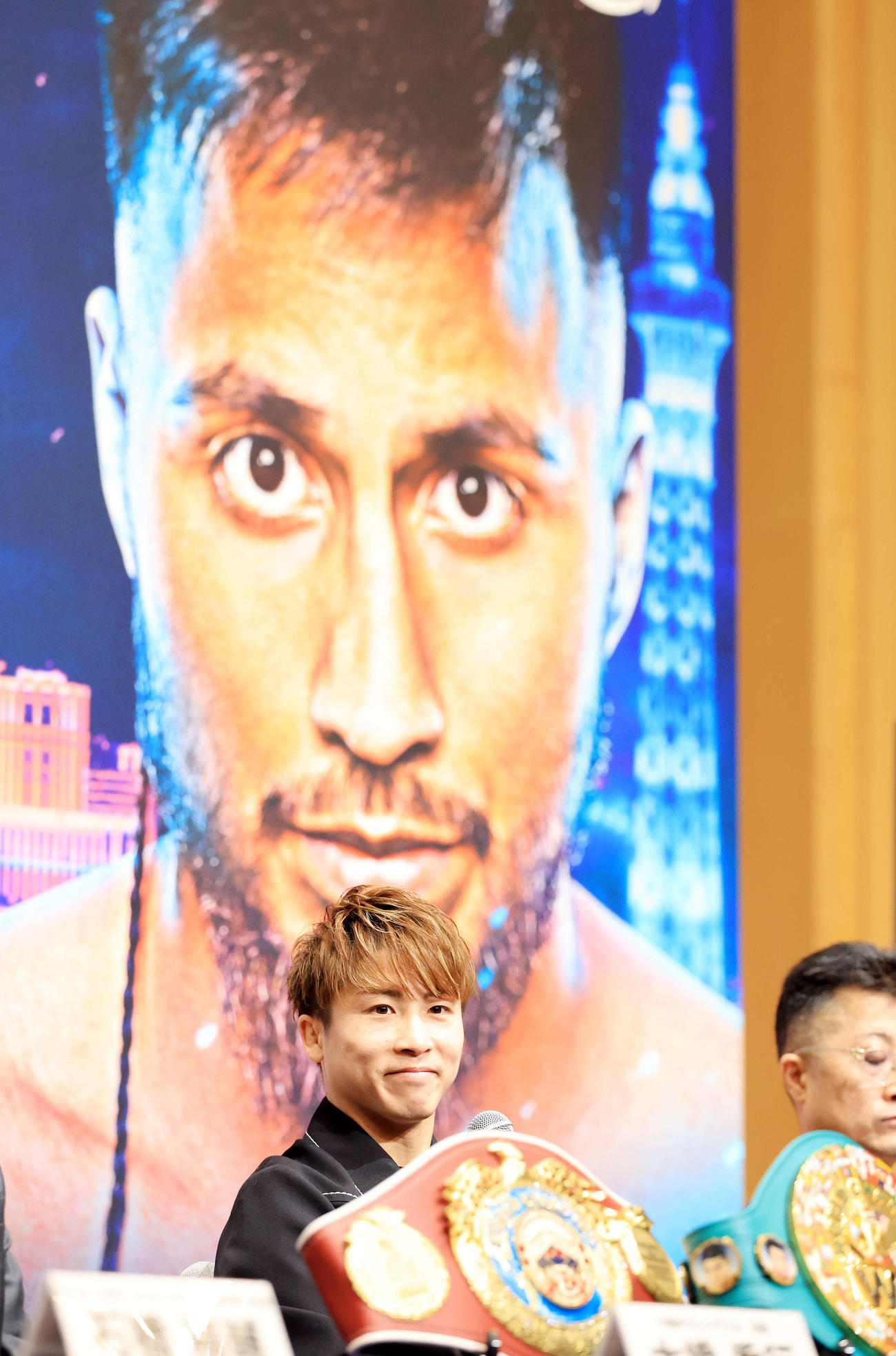 4団体統一世界スーパーバンタム級タイトルマッチ「井上尚弥　in　ラスベガス」の会見で対戦相手のラモン・カルデナスの写真を背に笑みを浮かべる井上（撮影・浅見桂子）