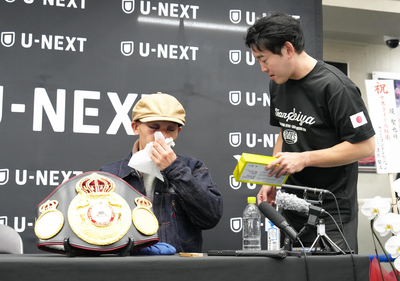 一夜明け、会見中、鼻の血を拭う堤（左）。右は石原トレーナー（撮影・足立雅史）