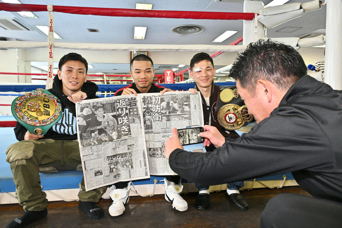 一夜明け会見で試合を報じる日刊スポーツを手にした、左から岩田、増田、松本の写真を撮る田中トレーナー（撮影・滝沢徹郎）