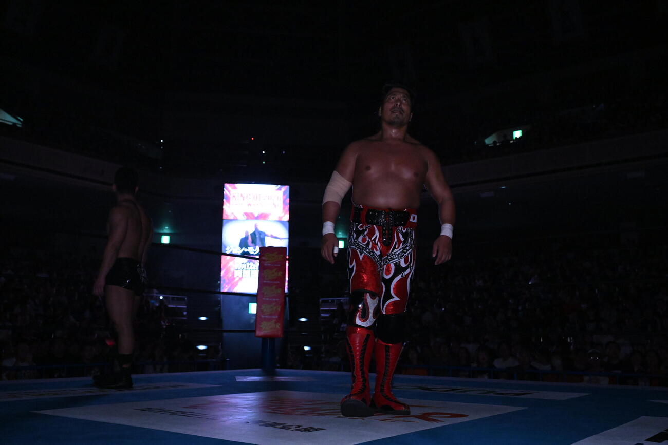 場内が暗転し、鷹木信悟の背後のスクリーンにジョン・モクスリーが現れた（C）新日本プロレス