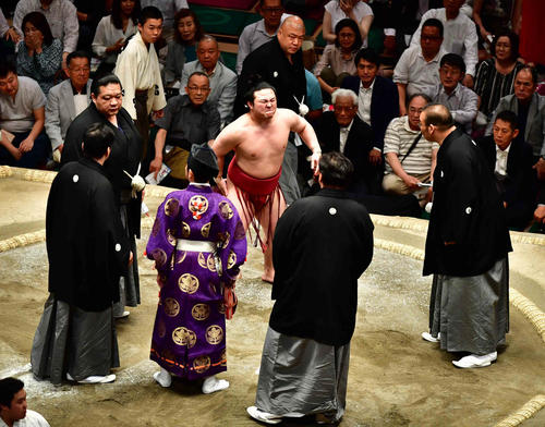 炎鵬（中央）は物言いが付き土俵上に審判団が集まるなか、取組で痛めた右足太もも裏の痛みに堪えながら土俵下への移動を試みる（撮影・小沢裕）