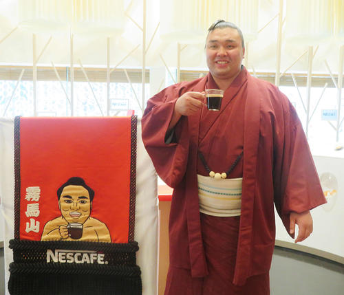 ネスレ日本から化粧まわしを贈呈され、化粧まわしのデザインと同じくコーヒーを飲む霧馬山（撮影・佐藤礼征）