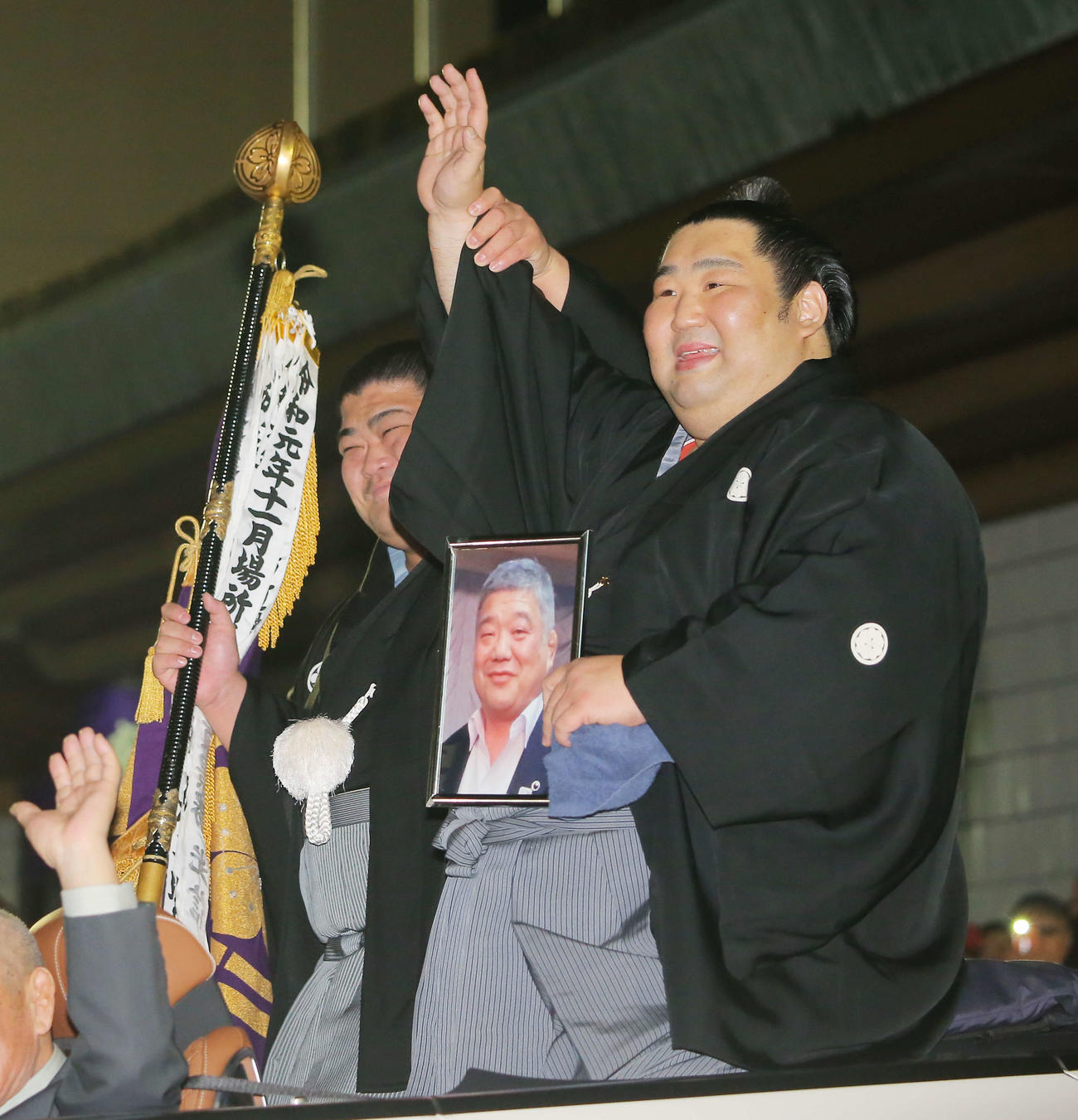 亡き恩師の近大相撲部伊東監督の遺影を手に、優勝パレード車から笑顔で手を振る徳勝龍（右）と旗持ちの志摩ノ海（撮影・河田真司）
