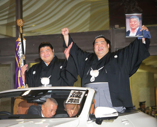 優勝パレードの車に乗り、亡き恩師の近大相撲部伊東監督の遺影を手にガッツポーズで満面の笑顔を見せる徳勝龍(右)と旗持ちの志摩ノ海(撮影・河田真司)